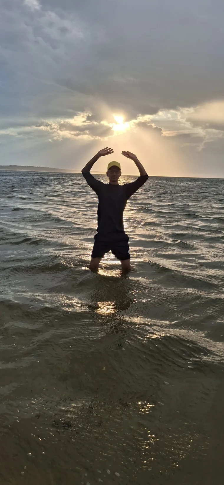Ernesto Hoyos practicando Tai Chi dentro del mar al atardecer, con los brazos en círculo sobre la cabeza